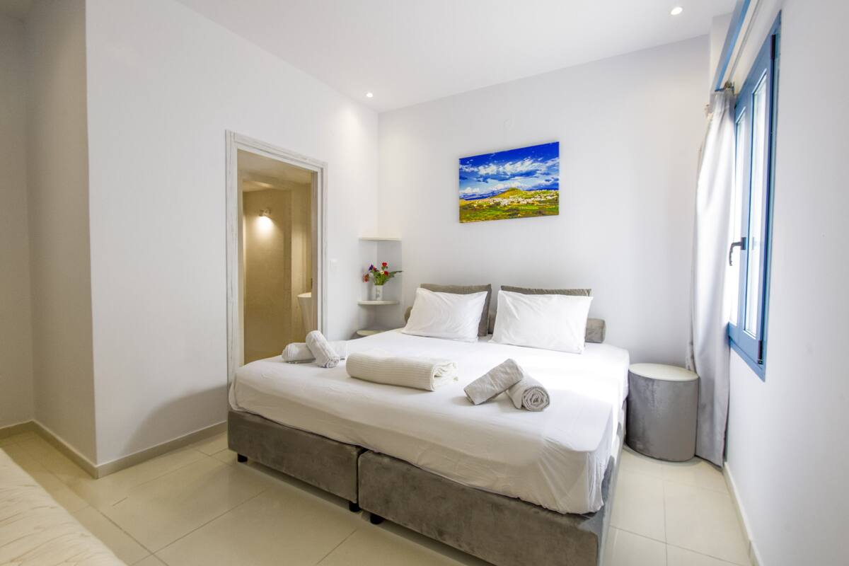 A modern bedroom with a large bed, a bedside table, a nightstand, and a painting on the wall.