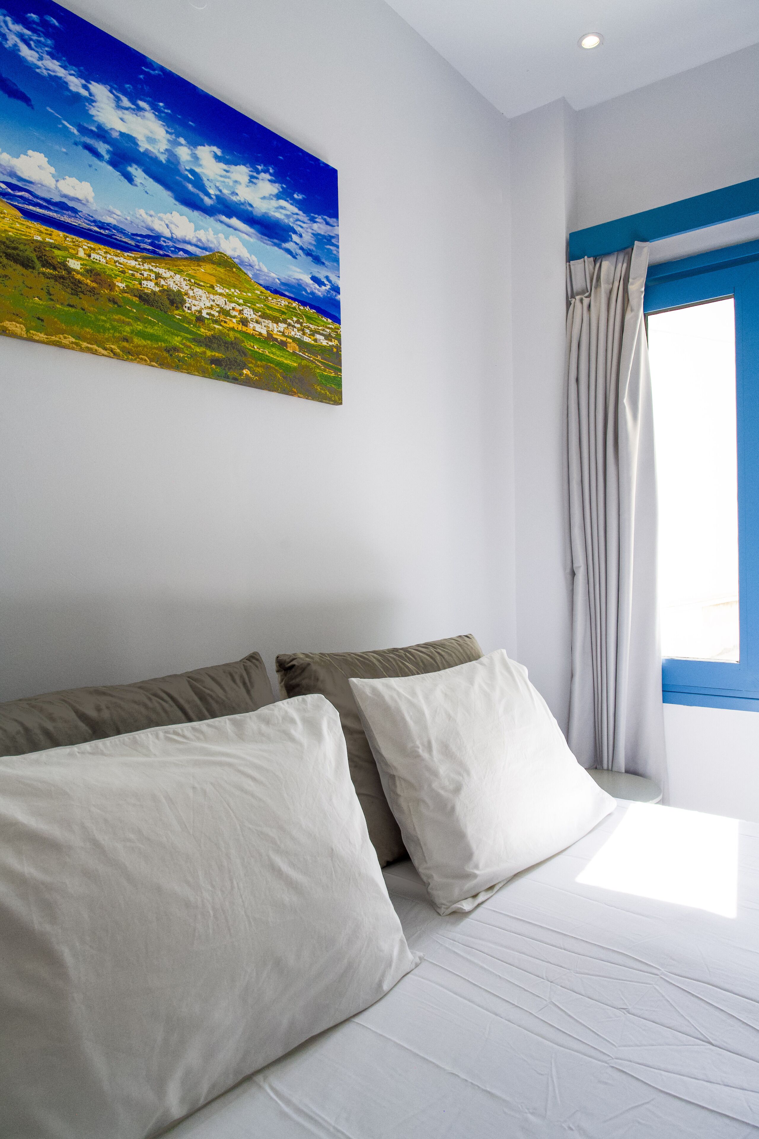 A bedroom with a bed, pillows, a painting, a window with curtains, and a view of a landscape.