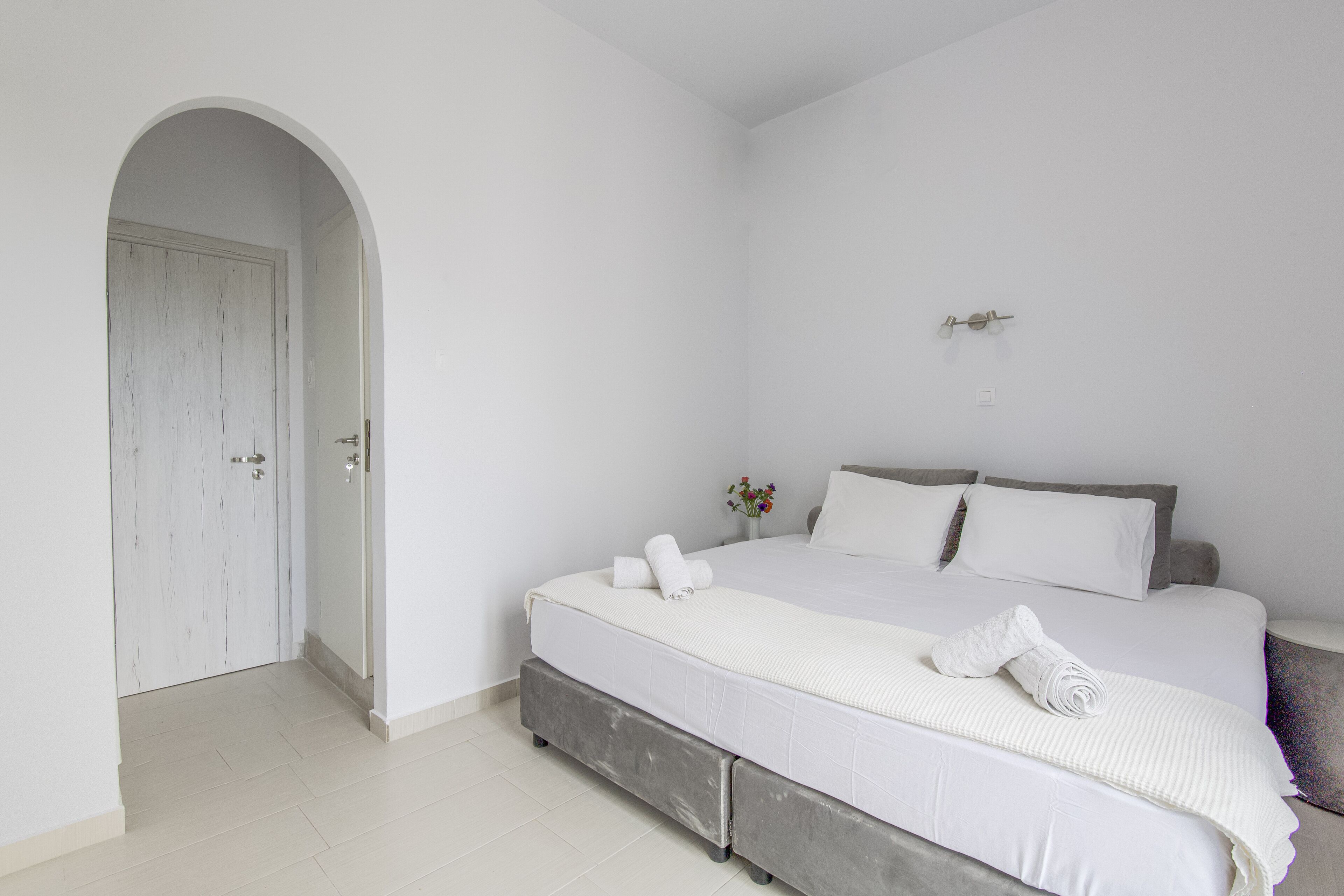 Une chambre avec un grand lit, une porte et une petite table ornée de fleurs.