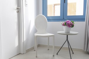 A white chair next to a small round table with a white vase containing purple flowers.
