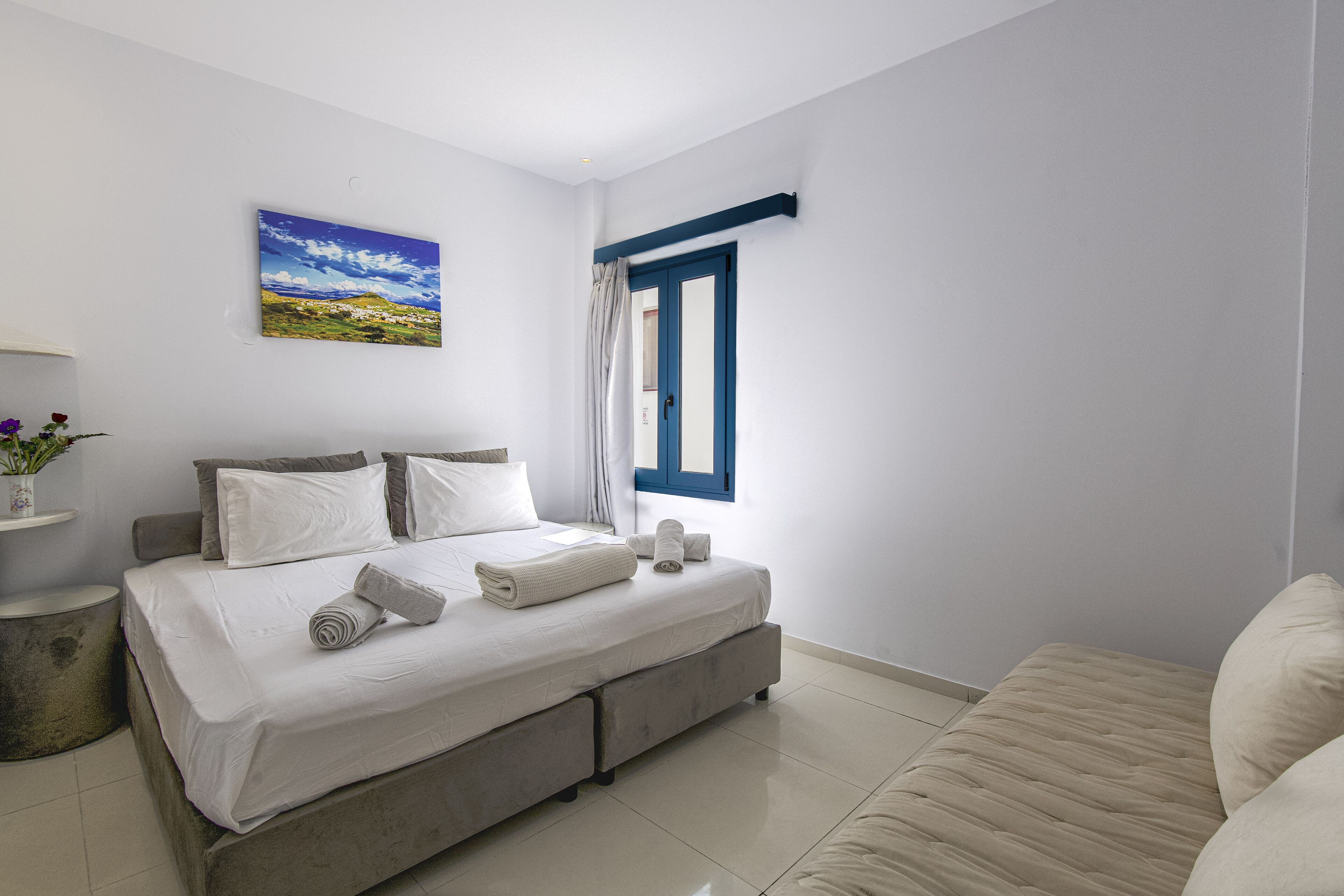 A bedroom with a bed, pillows, a window, and a painting on the wall.