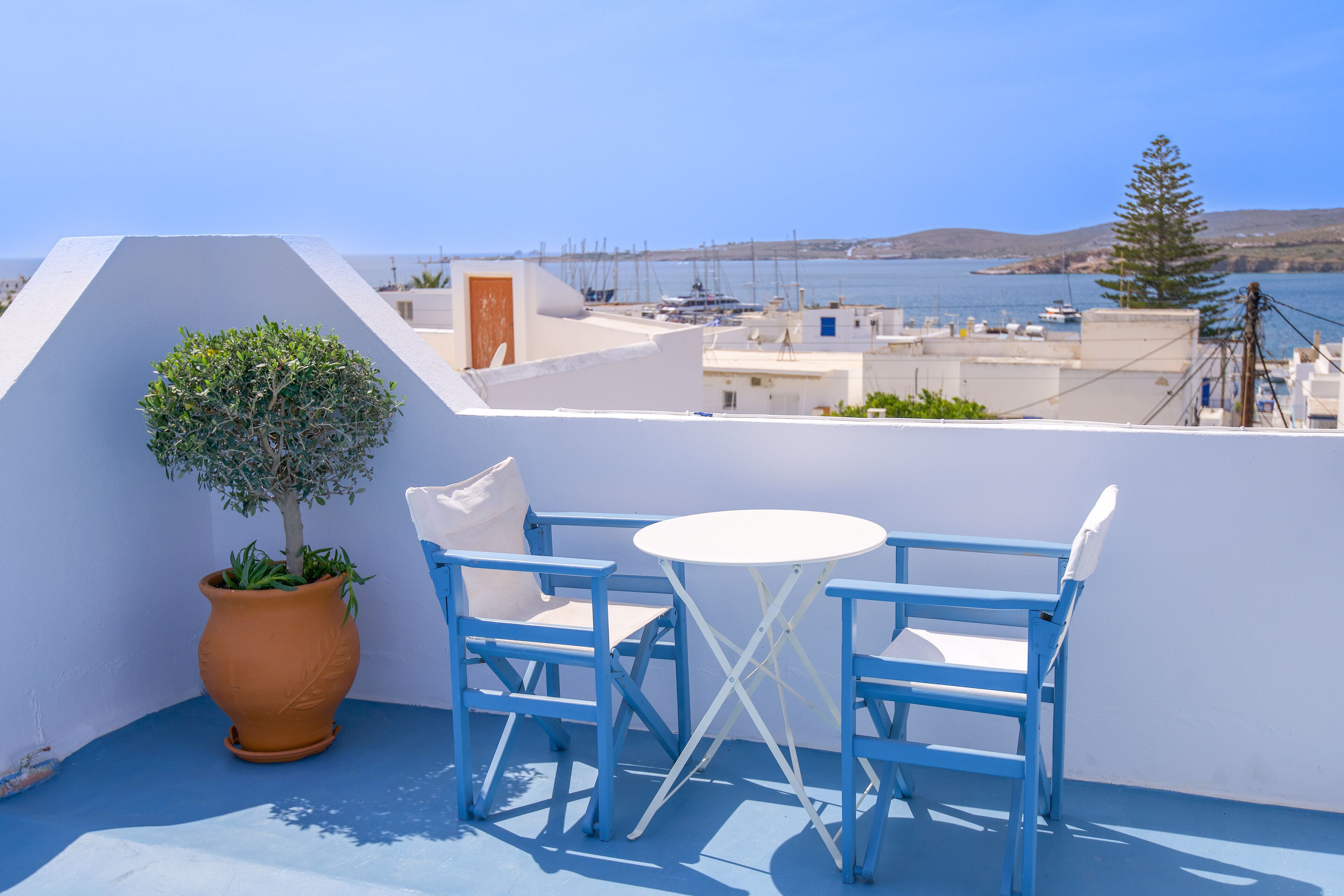 Una terraza con mobiliario azul, una mesa blanca y una planta en maceta.