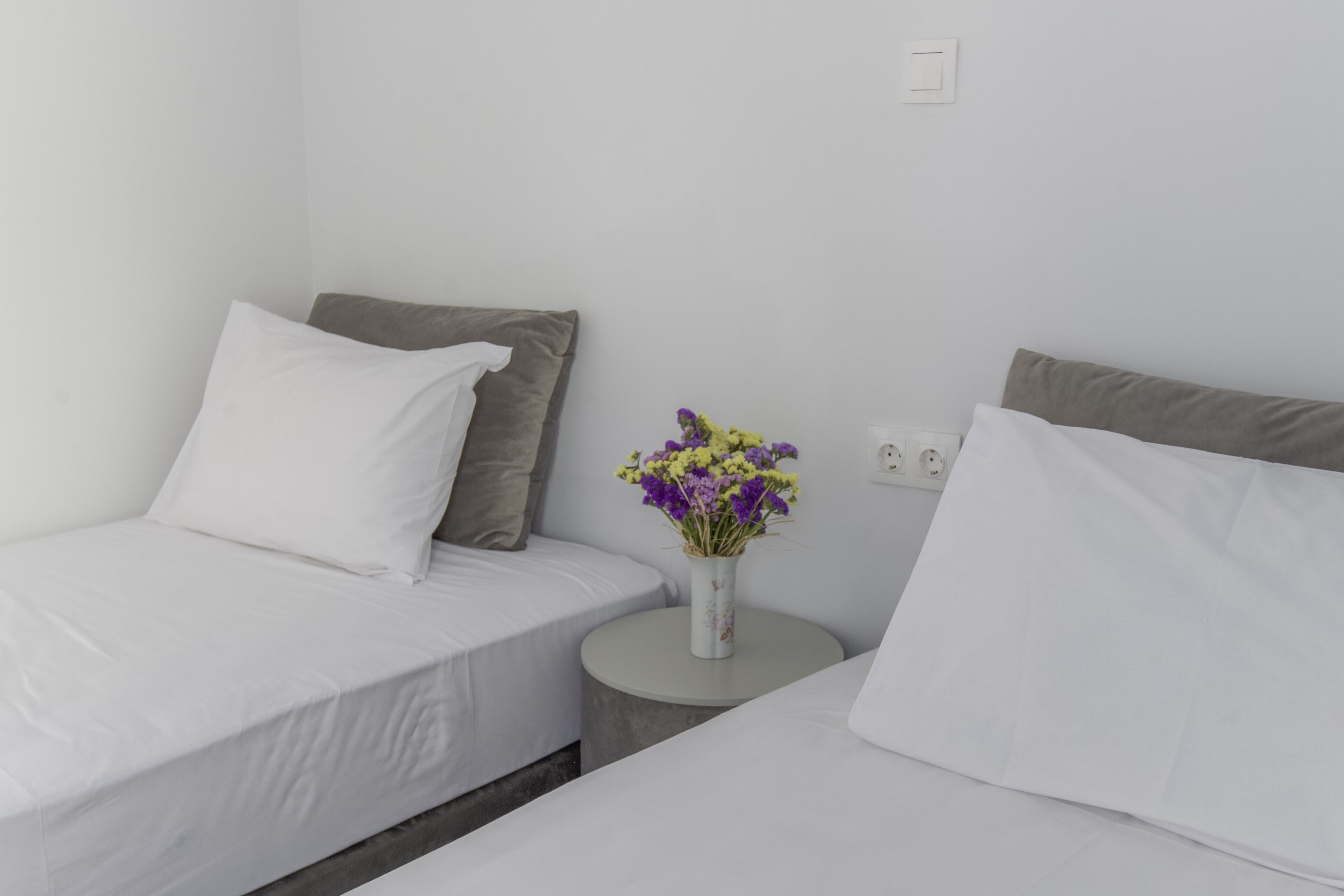 A room with two beds, a small round table with a vase of flowers, and a wall socket.