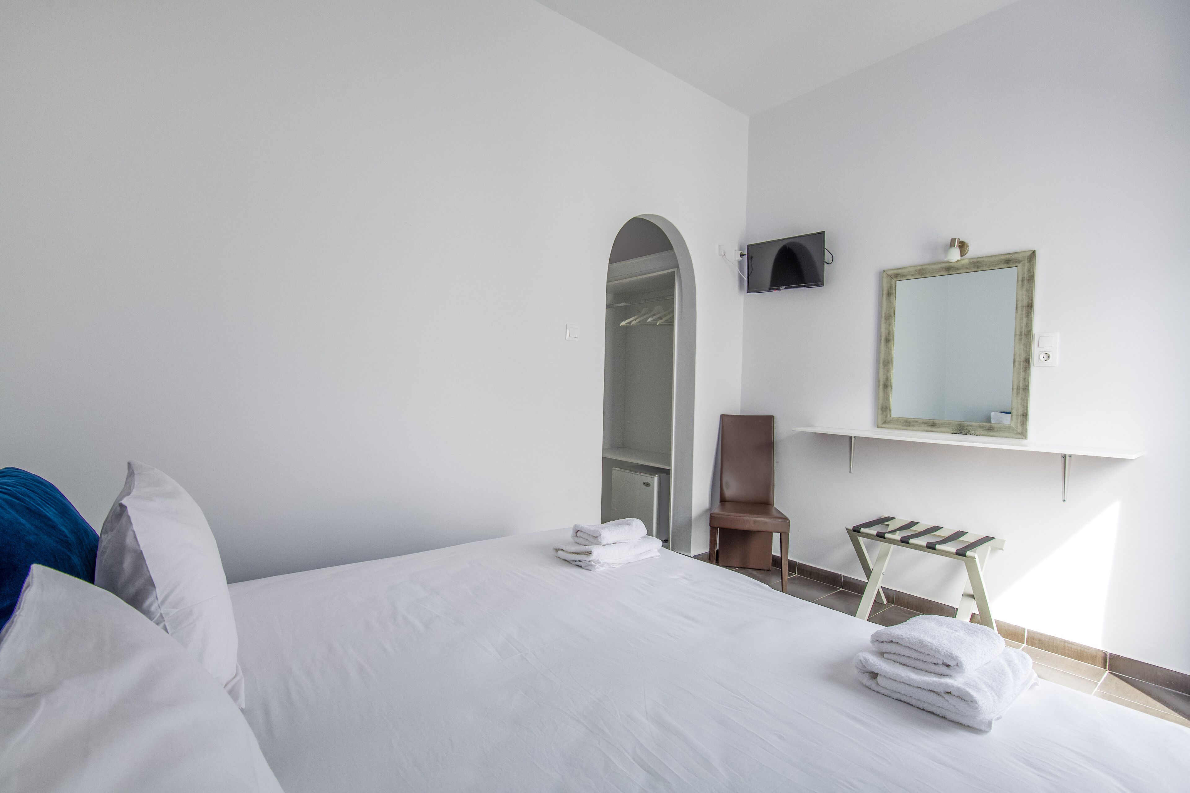 Habitación de hotel con cama, un taburete de madera, un espejo y un armario.