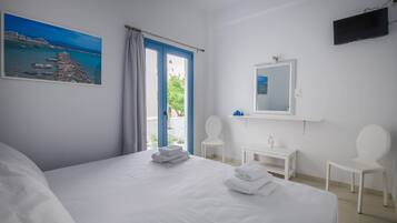 Ein Hotelzimmer mit einem Bett, einem Schreibtisch, zwei Stühlen, einem Fernseher, einem Gemälde und Meerblick durch ein Fenster.