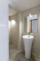A bathroom with a large white sink, a mirror, and a shower area.