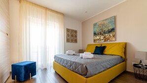 A modern bedroom with a large bed, a small blue ottoman, and artwork on the walls. - Casa ChiaLù by MONHOLIDAY (Monopoli)