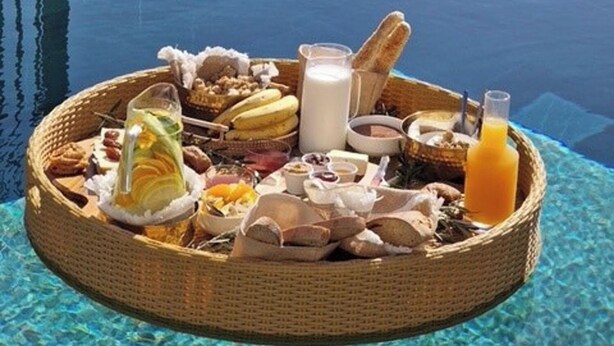 Ett brickbord med frukost placerat vid poolkanten, med olika sorters mat och dryck.