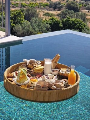 A breakfast tray on a poolside with various food items and drinks.