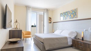 A modern hotel room with a large bed, a desk, a chair, and a view of the city through the window. - La stella sul mare by Monholiday (Monopoli)