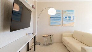 A modern living room with a flat-screen TV, a floor lamp, a small round table, and a beige sofa. There are two paintings on the wall depicting sailboats. - La stella sul mare by Monholiday (Monopoli)