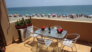 Una terraza con una mesa y sillas con vistas a una playa con sombrillas.
