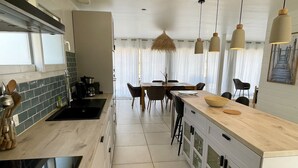 Eine moderne Küche mit einer zentralen Kochinsel, einem Essbereich mit Tisch und Stühlen sowie Pendelleuchten.