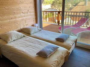 A room with two beds, a wooden wall, and a view of a deck and outdoor area.