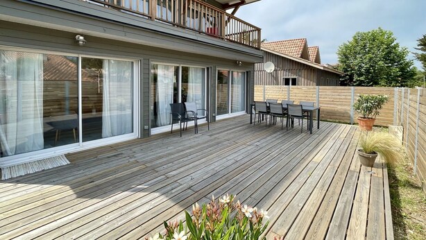 Ein zweistöckiges Haus mit Balkon, Schiebeglastüren und einer Holzterrasse.