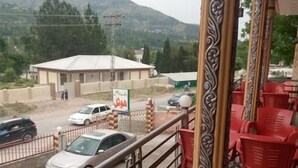A balcony with a metal railing, red plastic chairs, and a blue trash bin. - Balakot International Hotel (Balakot)