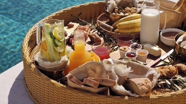 Een ontbijttafel met diverse etenswaren en drankjes bij een zwembad.