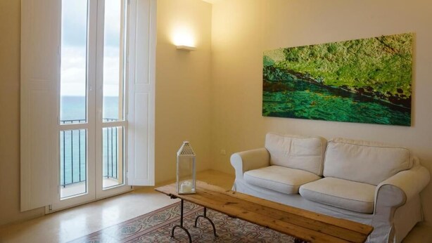 Una sala de estar con un sofá blanco, una mesa de centro de madera, un farol de cristal y un cuadro de un paisaje verde.