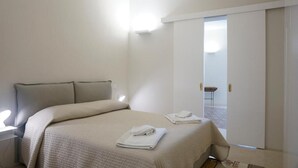Un dormitorio con cama, mesita de noche y puerta que da a un balcón.