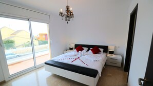 Un dormitorio con una cama grande, una araña y vistas a través de un ventanal corredero.