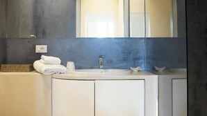 Un baño moderno con un tocador blanco curvo, un espejo grande y una cabina de ducha de vidrio.