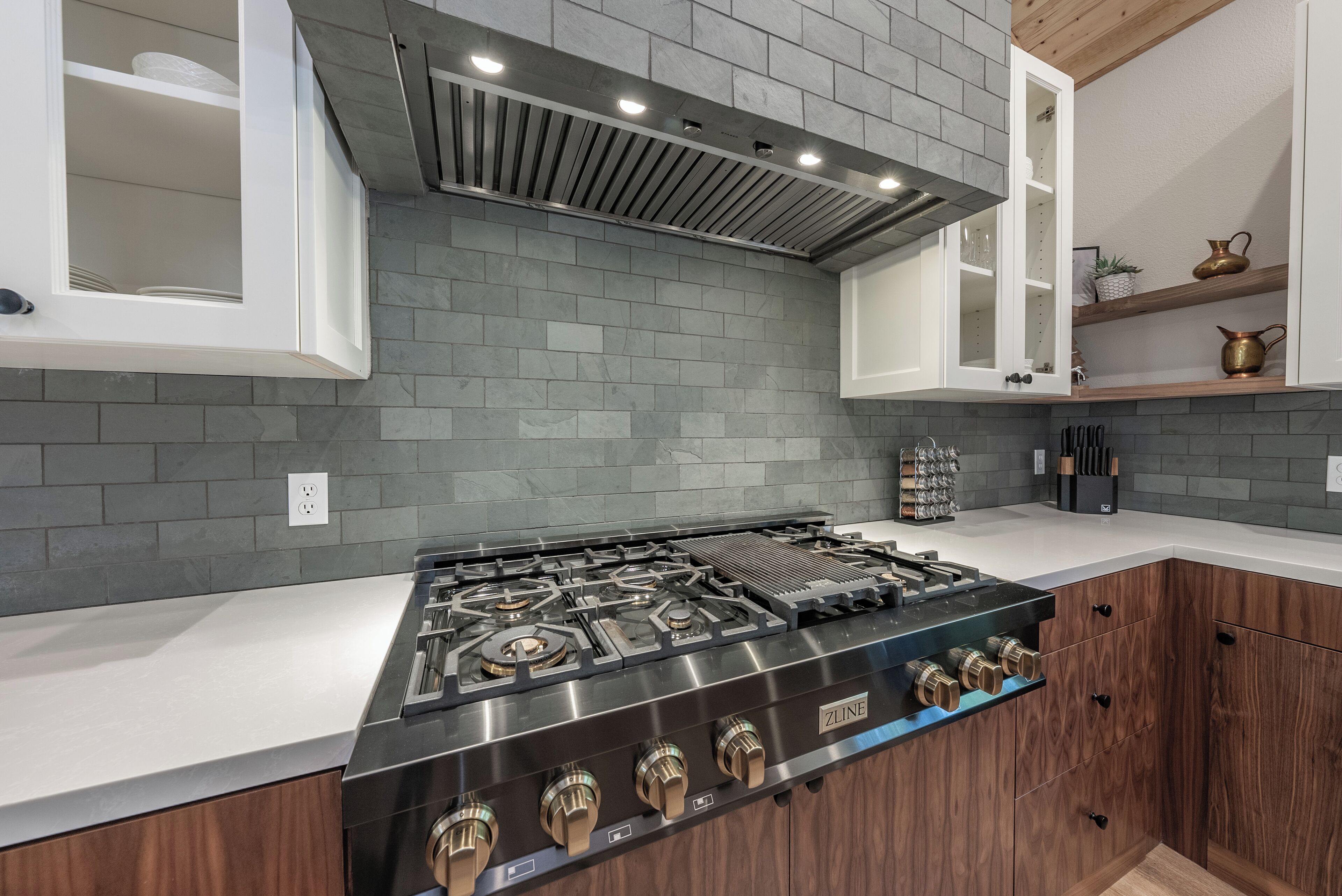 A modern kitchen with a stainless steel stove, wooden cabinets, and a grey tiled backsplash.