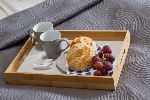 A wooden tray with a pastry, two cups, and grapes on a textured fabric surface.