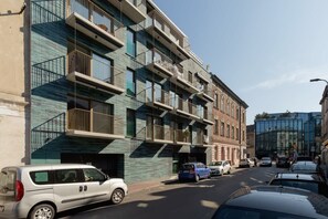 Ein mehrstöckiges Wohngebäude mit Balkonen, parkenden Autos und blauem Himmel.