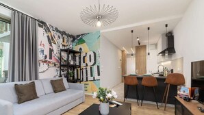 Una sala de estar moderna con un sofá gris, una mesa de centro negra y un mural abstracto de colores en la pared.
