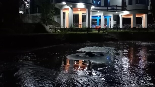 Een modern meerlaags gebouw met verlichte balkons en een reflecterend waterpartij ervoor.