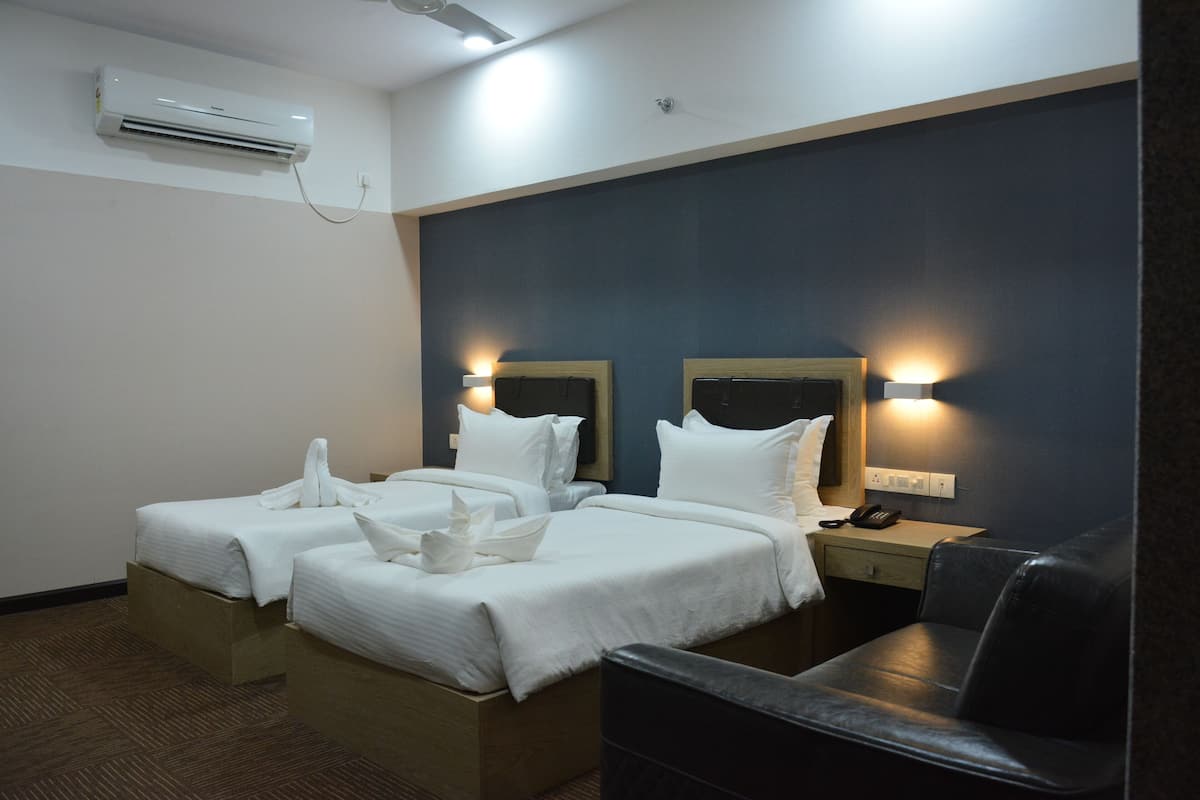 A hotel room with two beds, a desk, a chair, an air conditioning unit, and a wall-mounted lamp.