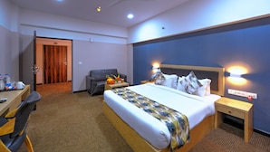 A hotel room with a bed, bedside table, nightstand, desk, chair, and a ceiling fan. - TreeHouse Morina (Mandal)