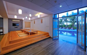 Amplia habitación con piso de madera, una gran mesa lista para comer, televisión y vista a una piscina a través de amplios ventanales.
