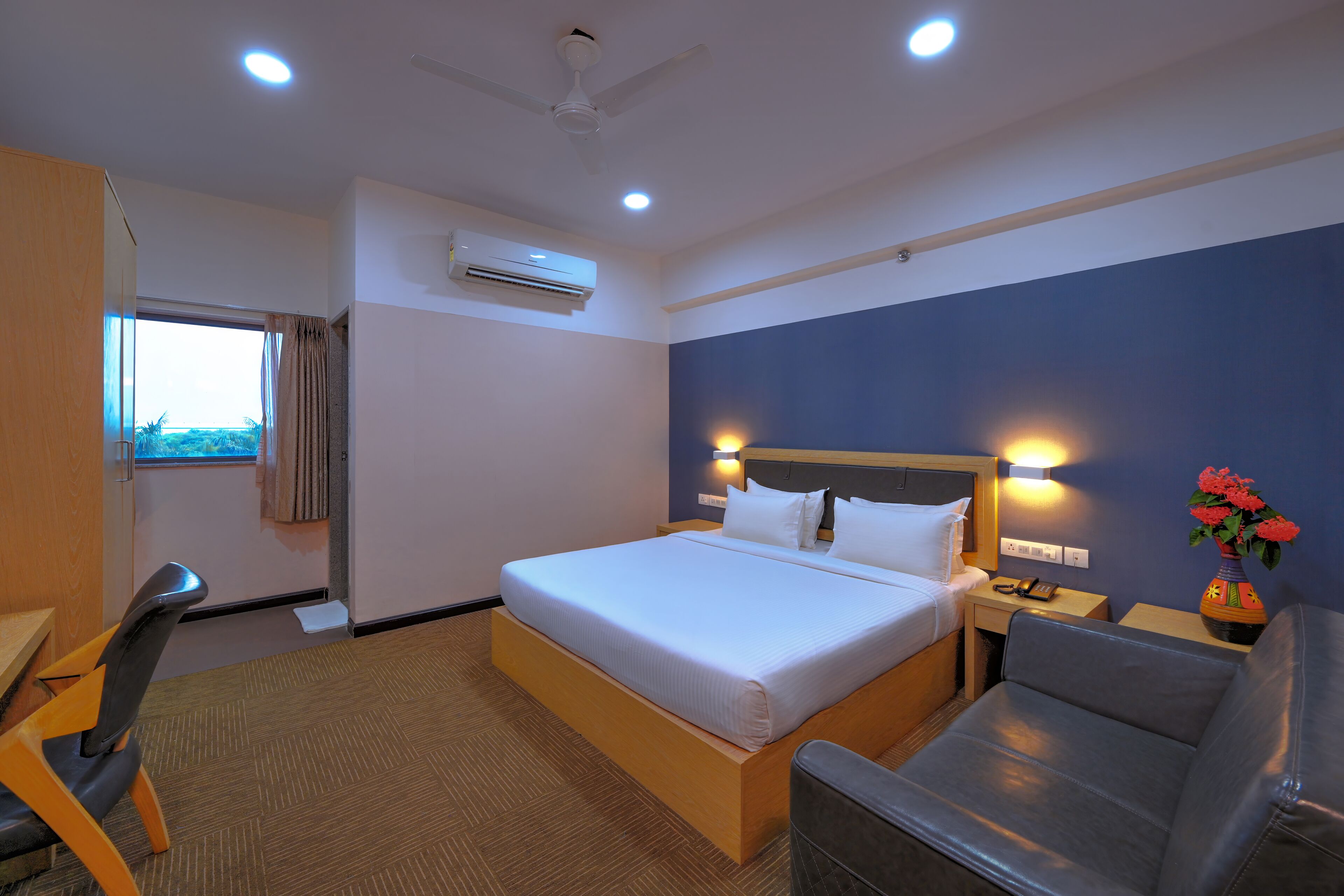 Habitación de hotel con cama, escritorio, silla, ventana, aire acondicionado y ventilador de techo.