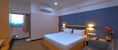 A hotel room with a bed, a desk, a chair, a window, an air conditioner, and a ceiling fan.