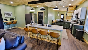 A modern kitchen with a central island, bar stools, and a dining area with a wooden table and chairs. - Best of the Smokies! •Game Room•GSMNP•Theater•Sleep 16•Hot Tub•Flat Parking (Sevierville)