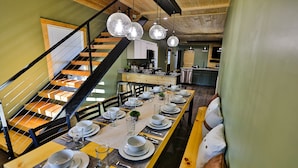 A dining area with a long wooden table set for a meal, a staircase with a black railing, and a kitchen in the background. - Best of the Smokies! •Game Room•GSMNP•Theater•Sleep 16•Hot Tub•Flat Parking (Sevierville)