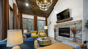 A modern living room with a fireplace, comfortable seating, and a large window. - Moroccan Nights|Hot Tub|Fire Pit|Hammocks (Broken Bow)