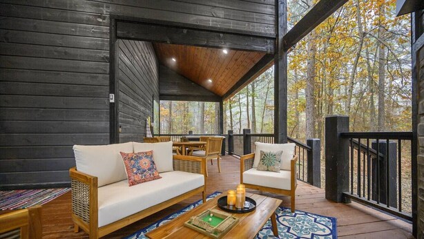 A covered outdoor seating area with a wooden deck, a sofa, a chair, and a table with candles. - Moroccan Nights|Hot Tub|Fire Pit|Hammocks (Broken Bow)