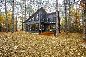 A modern cabin with a large deck, surrounded by a forest.
