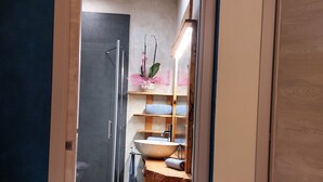 Un pasillo estrecho que conduce a un baño con tocador de madera, un espejo grande y una orquídea en maceta.