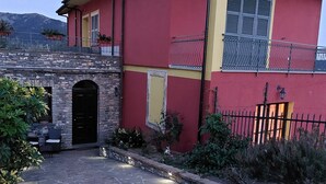Edificio rojo y amarillo con entrada de piedra, mesas al aire libre y un letrero que indica que es un restaurante.
