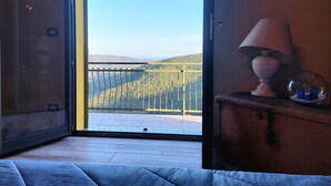 Una habitación con un ventanal grande, una cama, una lámpara y una pequeña mesa con un adorno.
