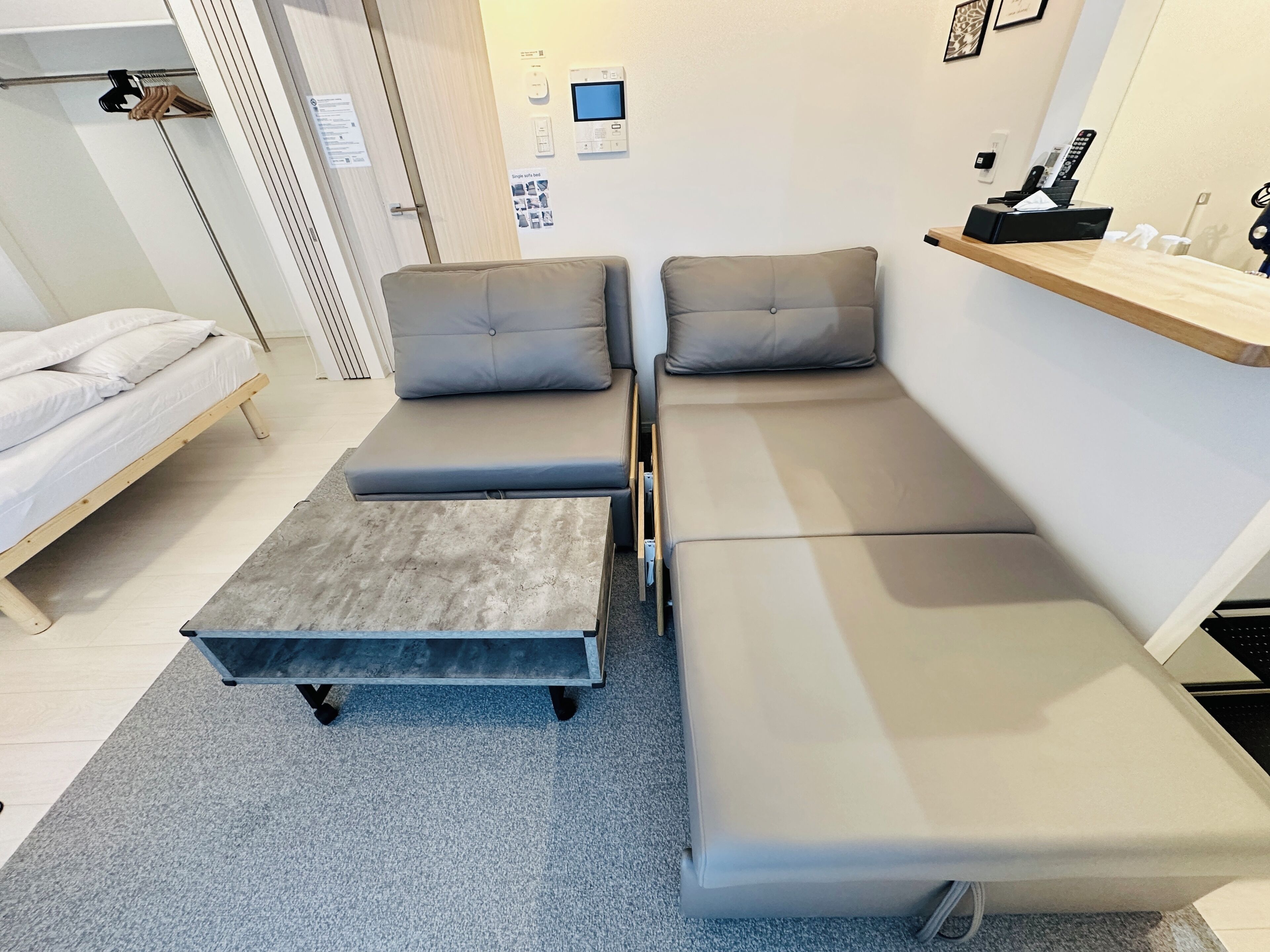 A compact room with a bed, two sofas, a small table, and a shelf with items.