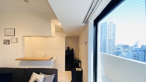 Una sala de estar moderna con un sofá, una mesa de centro y vistas a un paisaje urbano a través de un ventanal grande.