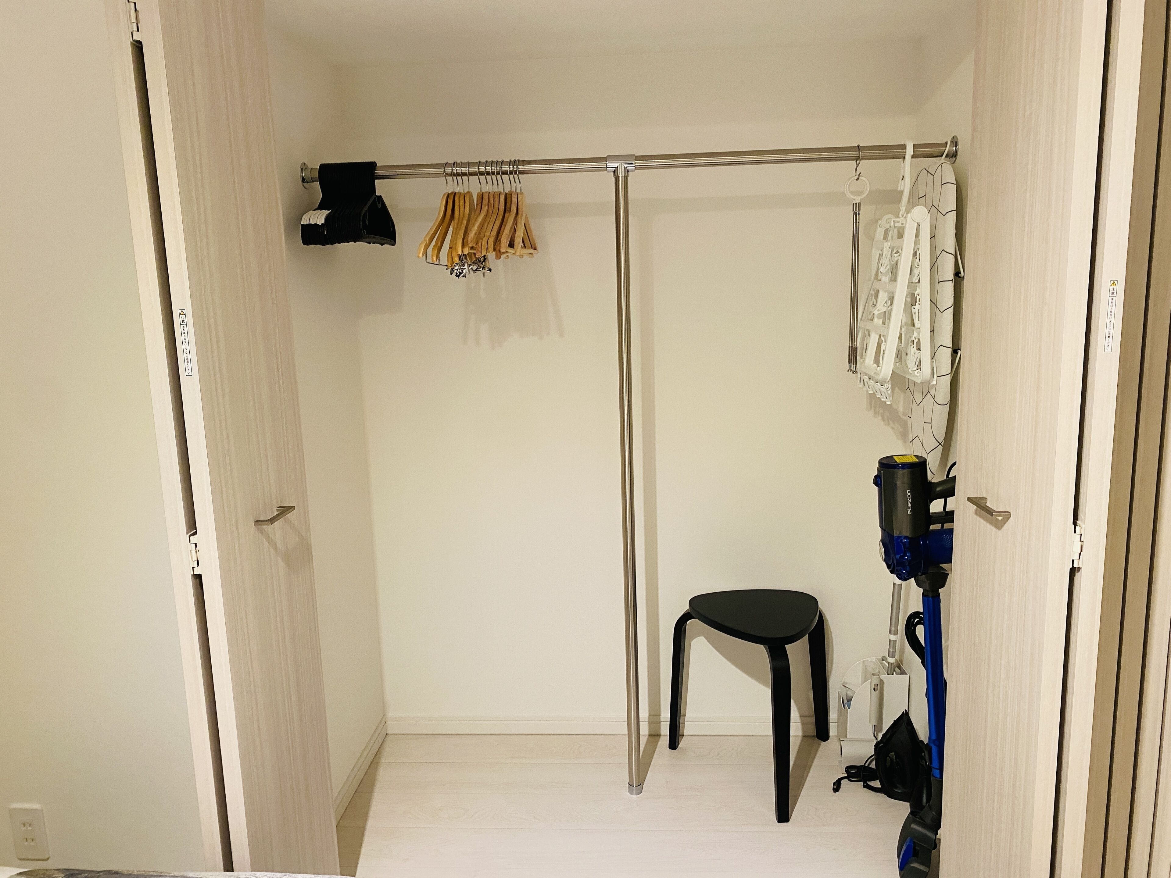A small, clean room with a wooden floor, a black chair, a drying rack with clothes, and a vacuum cleaner.