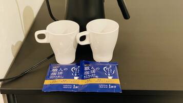 Une machine à café, deux tasses blanches et deux sachets de café sur une table noire.