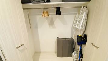 A compact storage closet with a hanging rack, a vacuum cleaner, and a storage bin.