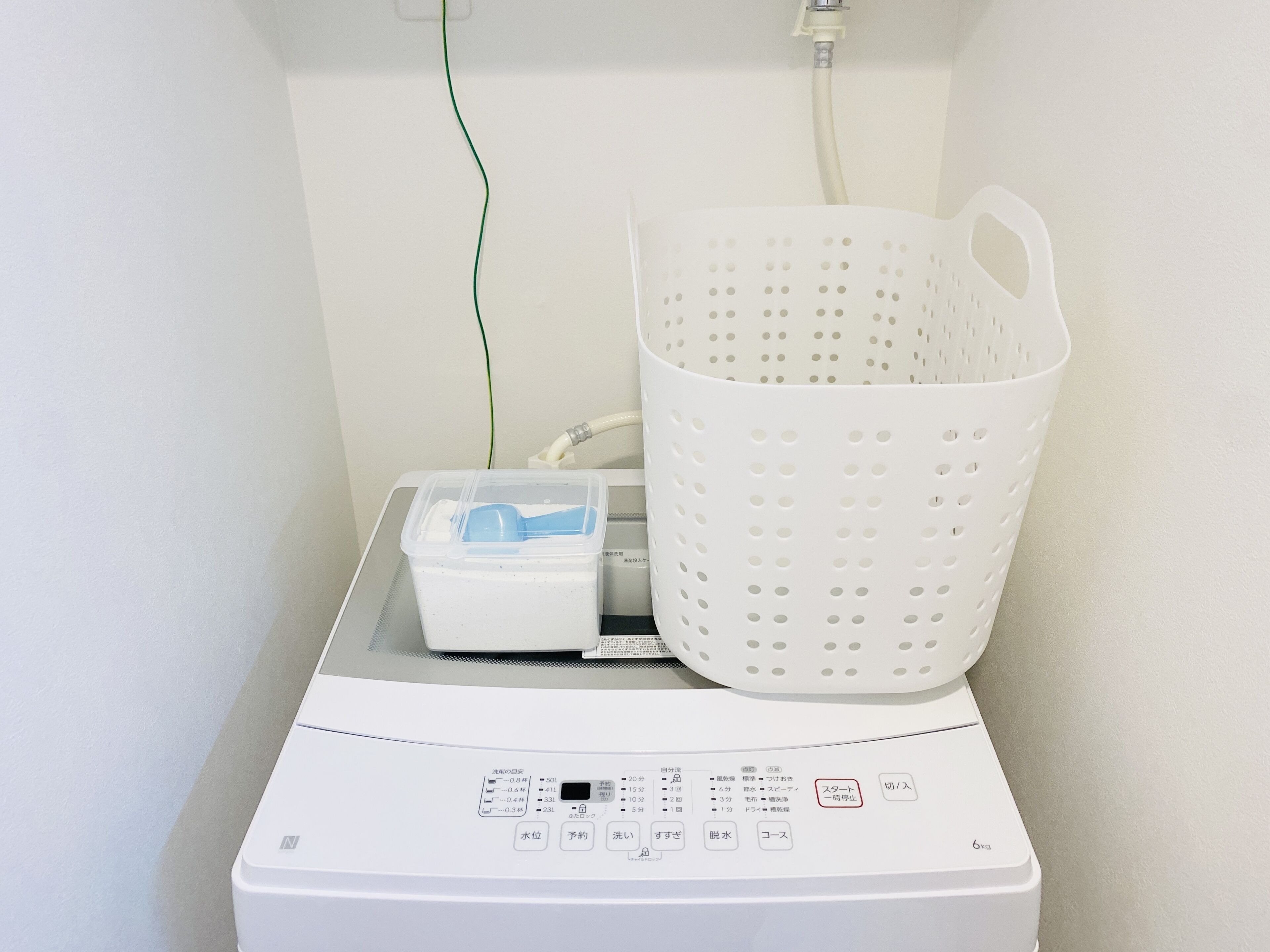 A laundry machine with a control panel, a plastic container, and a white laundry basket.