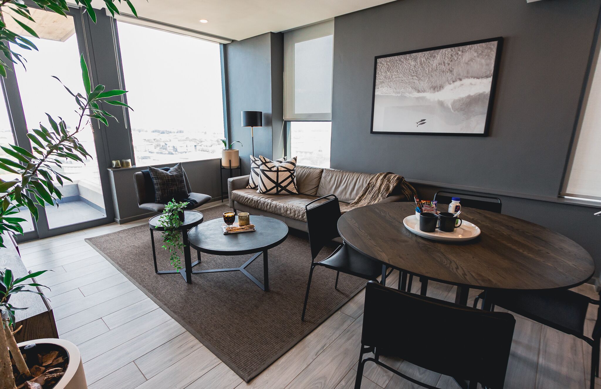 A modern living room with a sofa, two round tables, and a large window with a city view.